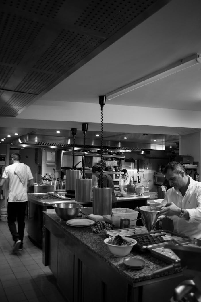 services-02 Black and white photo capturing chefs preparing dishes in a vibrant restaurant kitchen.