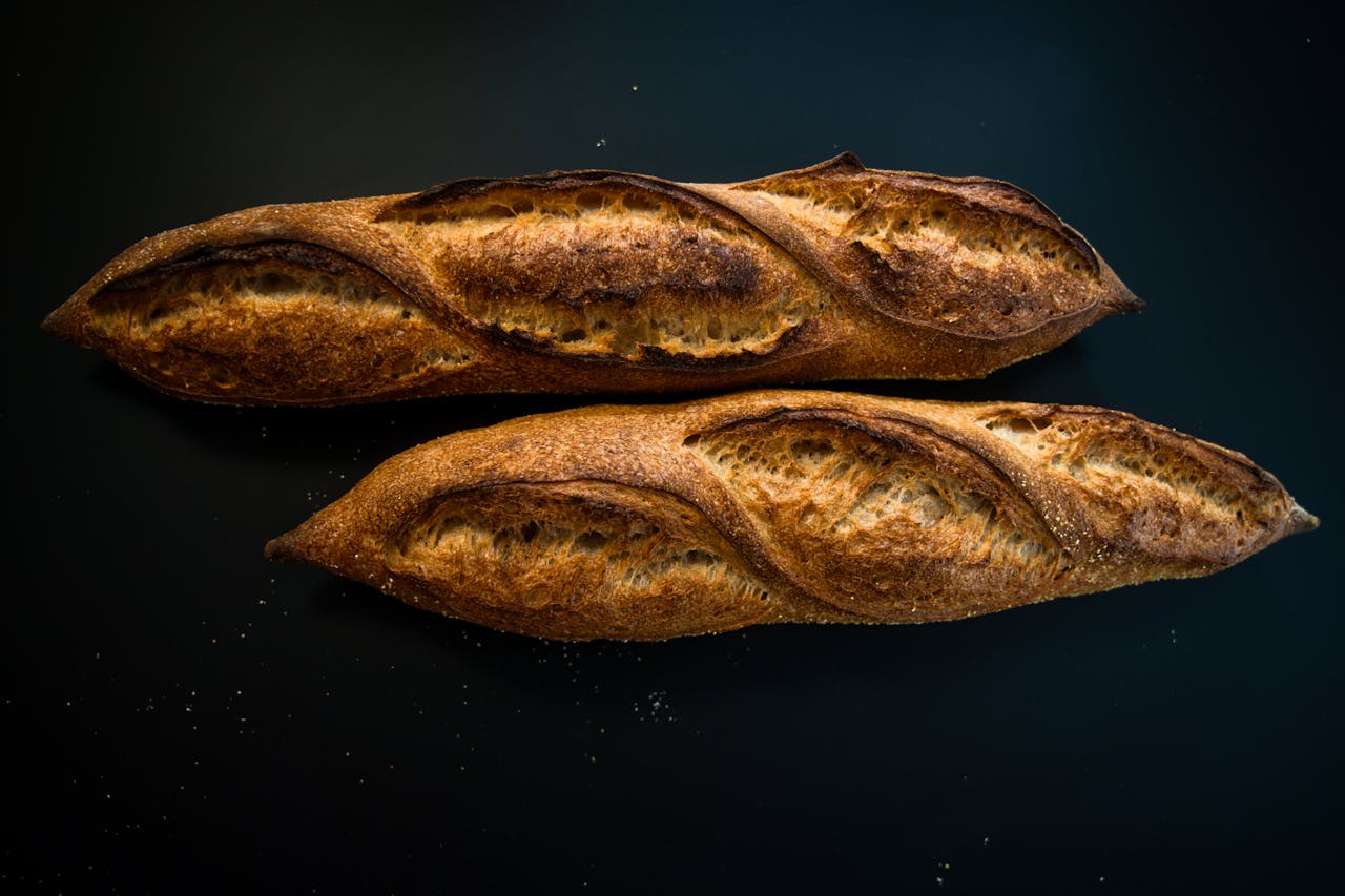 why-choose-us Close-up of two artisanal baguettes with rich textures on a dark surface, perfect for bakery themes.
