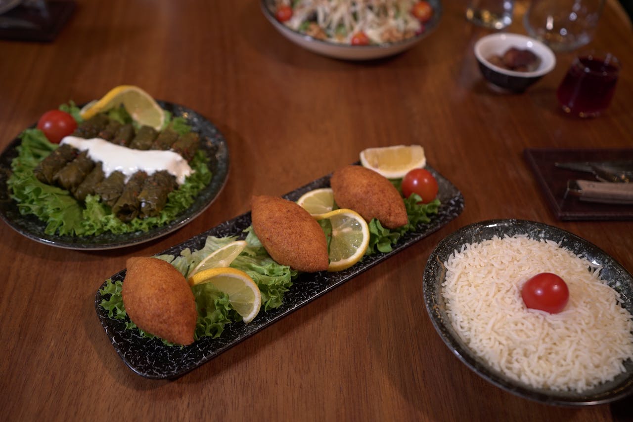 services-bg Delicious Middle Eastern dishes including kibbeh, dolma, and rice served with greens and lemon slices.